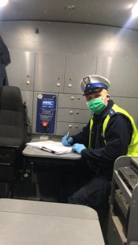 Policjant sporządza dokumentację w radiowozie w maseczke i rękawiczkach ochronnych