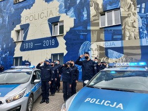Policjanci przy radiowozach na tle policyjnego muralu