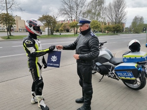 policjant ruchu drogowego rozmawia z zatrzymanym do kontroli motocyklistą i wręcza mu upominek