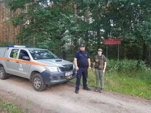 Pani strażnik Leśny oraz policjant stoją przy znaku informującym o obszarze chronionym natura 2000