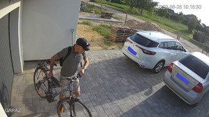 mężczyzna w czapce w koszulce z krótkim rękawem kradnie rower z posesji.