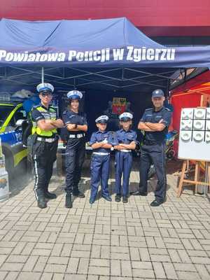 policjanci na stoisku promocyjnym z dziećmi przebranymi za policjantów ruchu drogowego