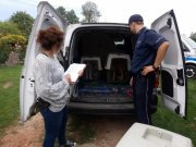 policjant w mundurze i policjantka po cywilnego stoją przy części bagazowej auta , w której znajdują się zabezpieczone w klatach transportowch psy  psy