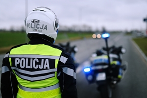 Policjant w mundurze, w tle motocykl służbowy.