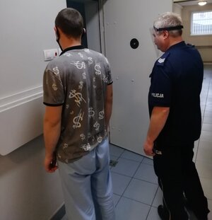 korytarz komendy policji, umundurowany policjant prowadzi zatrzymanego mężczyznę