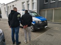 Policjant prowadzi zatrzymanego mężczyznę do radiowozu.