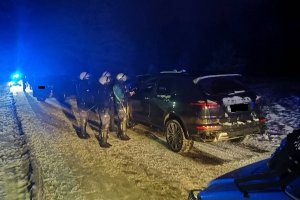 ośnieżona droga po zmierzchu, policjanci z oddziału prewencji kontrolują czarnego suv-a