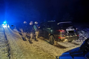 ośnieżona droga po zmierzchu, policjanci z oddziału prewencji kontrolują czarnego suv-a
