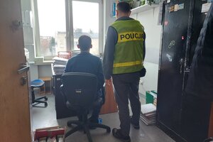 Pokój w komendzie policji, nieumundurowany policjant wykonuje czynności z zatrzymanym mężczyzną