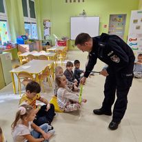 policjant rozdaje dzieciom w przedszkolu opaski odblaskowe.