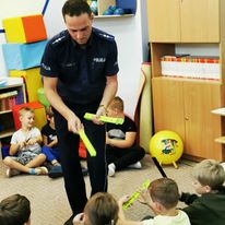 policjant rozdaje dzieciom w przedszkolu opaski odblaskowe.