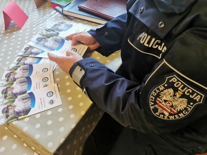 policjant trzyma ulotki z kampanii pod nazwą a kto tu się podszywa podczas spotkania z seniorami.