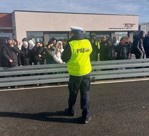 część praktyczna spotkania z młodzieżą która odbywa się na zewnątrz budynku, policjant rozmawia z uczniami szkoły podstawowej.