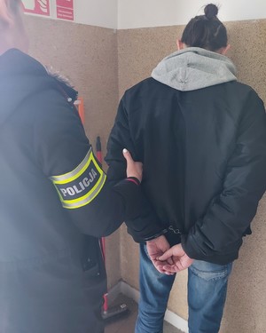 Zatrzymany mężczyzna pilnowany przez policjanta.