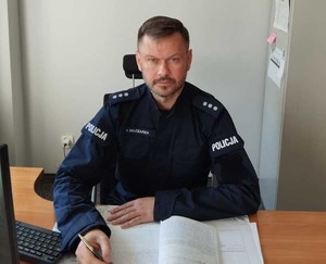 Policjant w mundurze siedzi za biurkiem w ręku trzyma długopis.