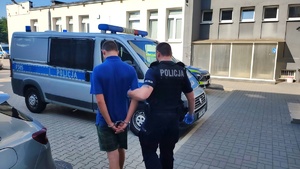 Policjant prowadzi zatrzymanego do radiowozu