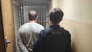 Umundurowany policjant prowadzi zatrzymanego mężczyznę do policyjnej celi